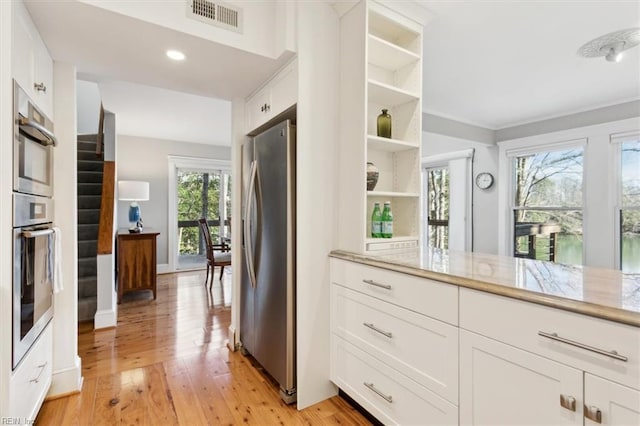 kitchen with light stone counters, stainless steel appliances, light hardwood / wood-style flooring, and white cabinetry