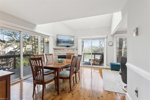 dining room with vaulted ceiling, a fireplace, and light hardwood / wood-style floors