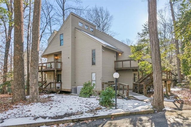 snow covered house with a balcony, a wooden deck, and central air condition unit