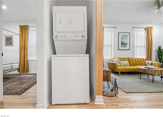 laundry room featuring ceiling fan, stacked washer and dryer, and light hardwood / wood-style floors