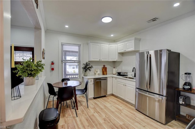 kitchen featuring white cabinets, stainless steel appliances, decorative backsplash, sink, and ornamental molding