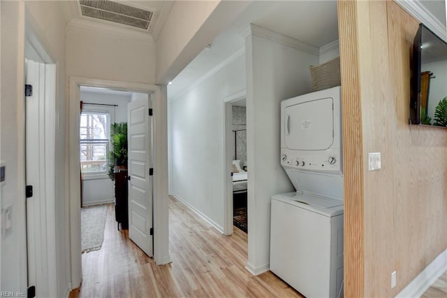 laundry area with stacked washer and clothes dryer, ornamental molding, and light hardwood / wood-style floors