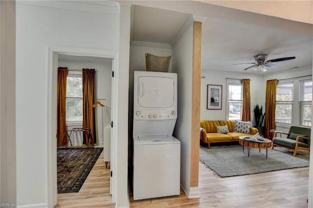 washroom with light hardwood / wood-style floors, stacked washer / drying machine, crown molding, and ceiling fan