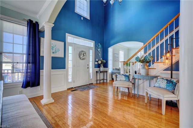 entrance foyer with an inviting chandelier, hardwood / wood-style flooring, decorative columns, a towering ceiling, and crown molding