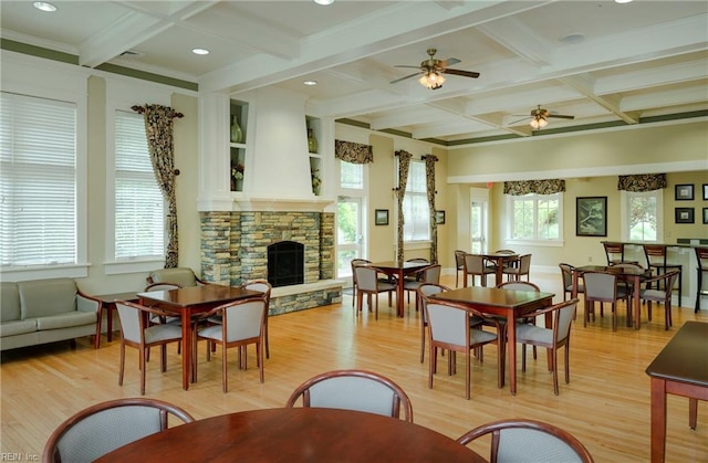 dining space with ceiling fan, a stone fireplace, coffered ceiling, and beamed ceiling