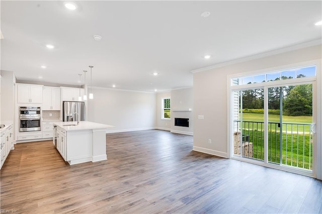 kitchen featuring hanging light fixtures, stainless steel appliances, a center island with sink, white cabinetry, and ornamental molding