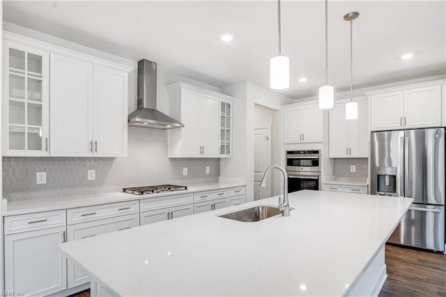 kitchen featuring a center island with sink, appliances with stainless steel finishes, wall chimney exhaust hood, sink, and white cabinetry