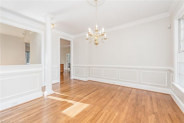 spare room featuring ornamental molding, hardwood / wood-style floors, decorative columns, and a chandelier