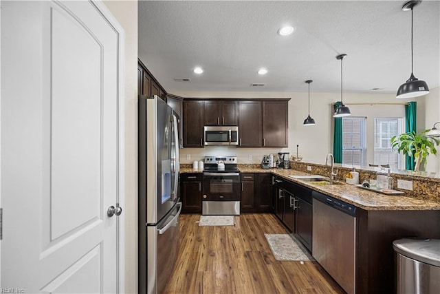 kitchen with stainless steel appliances, kitchen peninsula, sink, dark brown cabinets, and decorative light fixtures