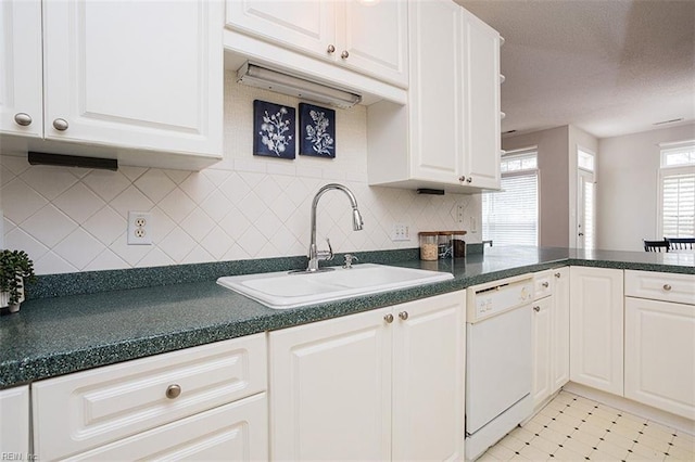 kitchen featuring white dishwasher, white cabinets, backsplash, and sink