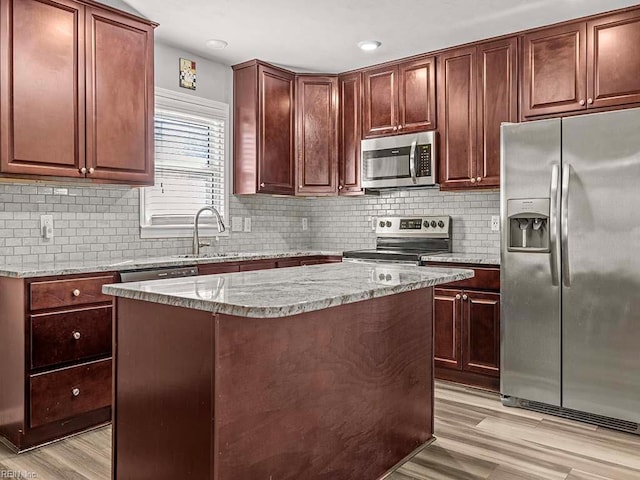 kitchen featuring sink, light stone counters, a center island, appliances with stainless steel finishes, and light hardwood / wood-style floors