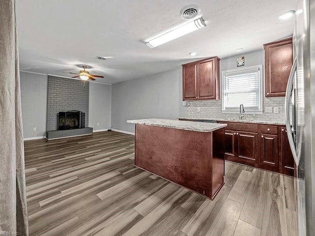 kitchen featuring stainless steel fridge, decorative backsplash, a kitchen island, a brick fireplace, and ceiling fan