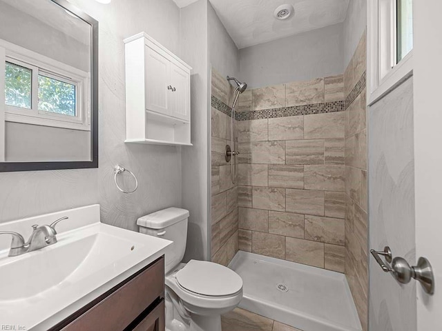 bathroom with toilet, a tile shower, and vanity