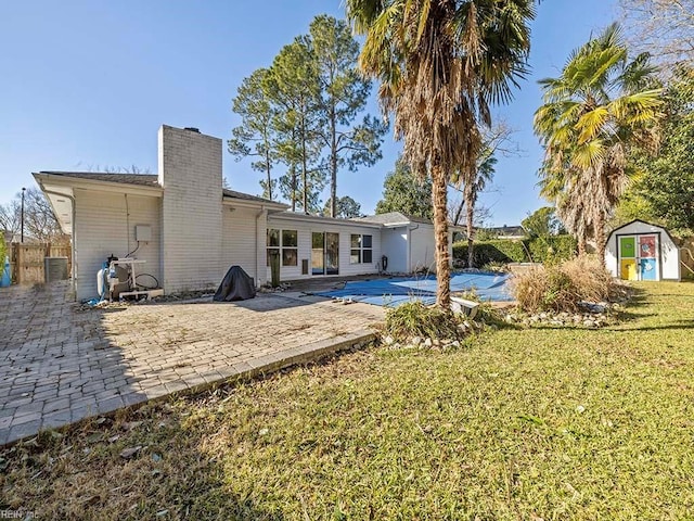 rear view of house with central air condition unit, a covered pool, a lawn, a patio, and a shed