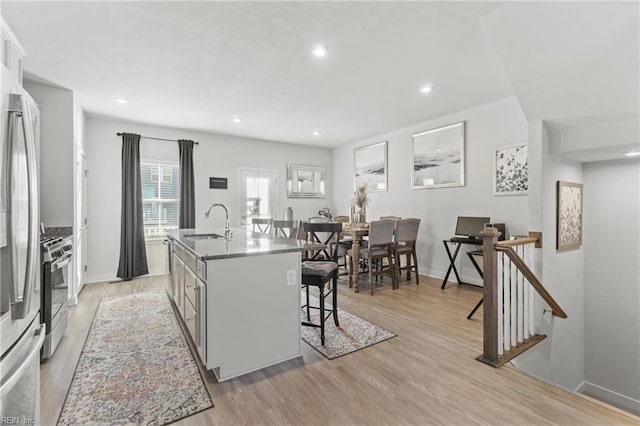 kitchen with stainless steel appliances, a center island with sink, a breakfast bar, light wood-type flooring, and sink