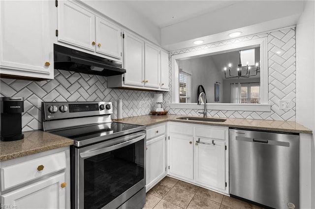 kitchen with white cabinetry, stainless steel appliances, dark stone counters, sink, and a notable chandelier