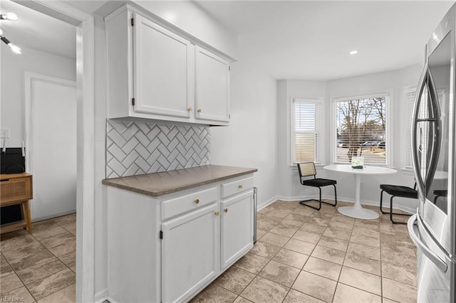 kitchen with white cabinets, backsplash, stainless steel fridge, and light tile patterned flooring