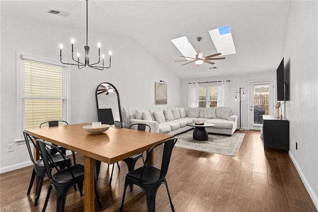 dining room with vaulted ceiling with skylight, ceiling fan with notable chandelier, and dark hardwood / wood-style flooring