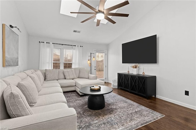 living room with ceiling fan, vaulted ceiling with skylight, and dark wood-type flooring