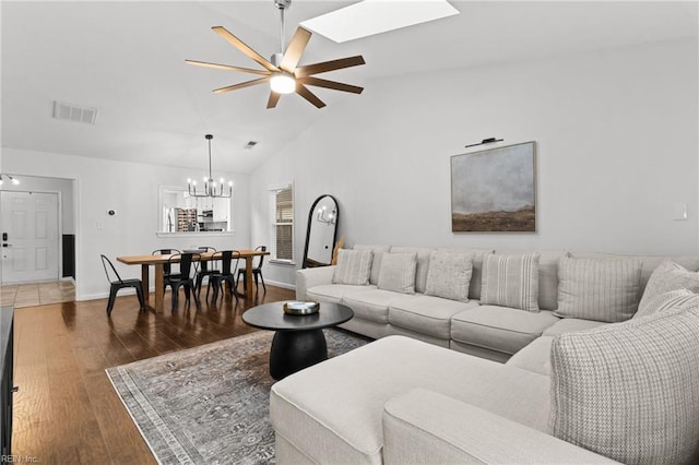 living room with vaulted ceiling with skylight, dark hardwood / wood-style floors, and ceiling fan with notable chandelier