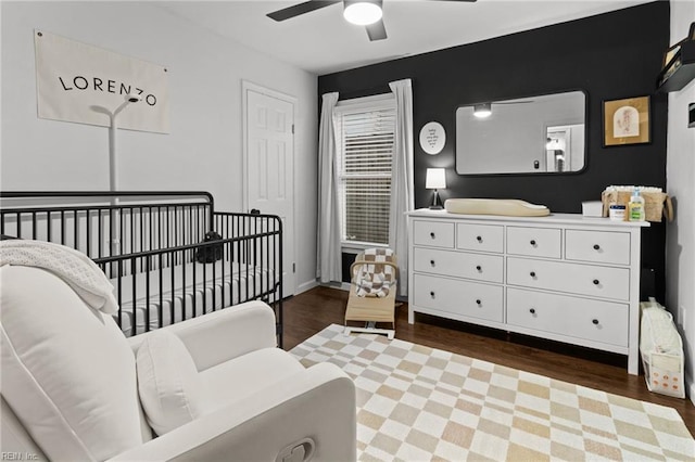 bedroom with ceiling fan, dark hardwood / wood-style floors, and a crib