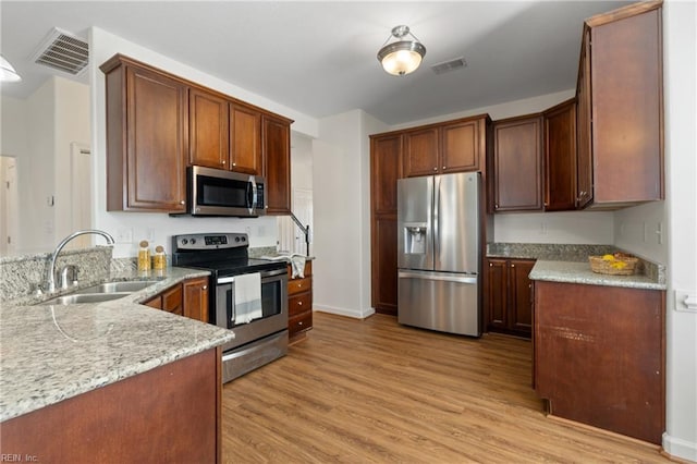 kitchen featuring appliances with stainless steel finishes, light hardwood / wood-style flooring, light stone counters, and sink