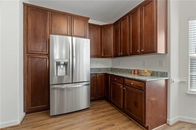 kitchen with light wood-type flooring, stainless steel fridge with ice dispenser, and dark stone counters