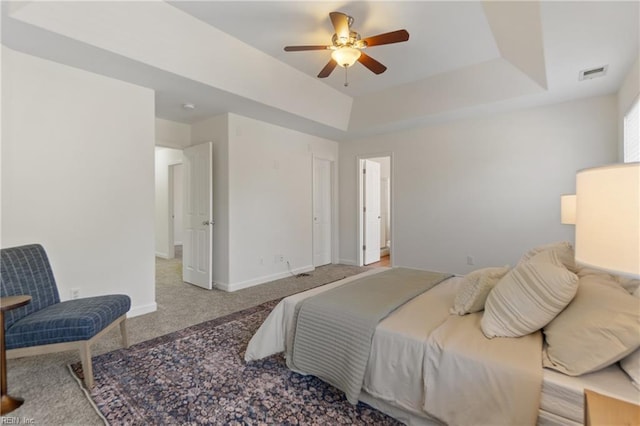 carpeted bedroom with a raised ceiling and ceiling fan