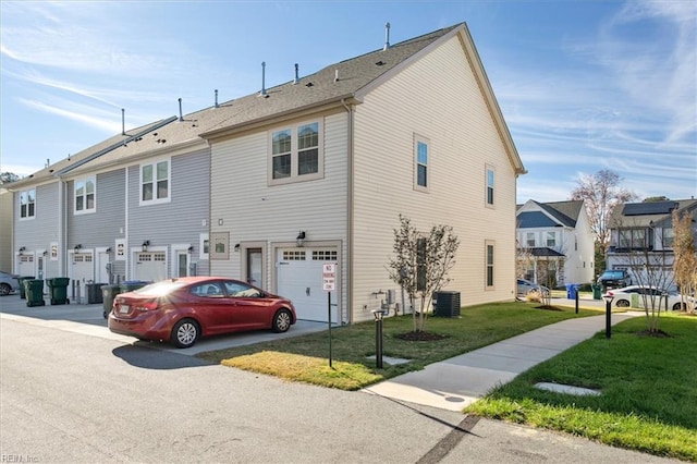 rear view of property featuring a yard, central AC unit, and a garage