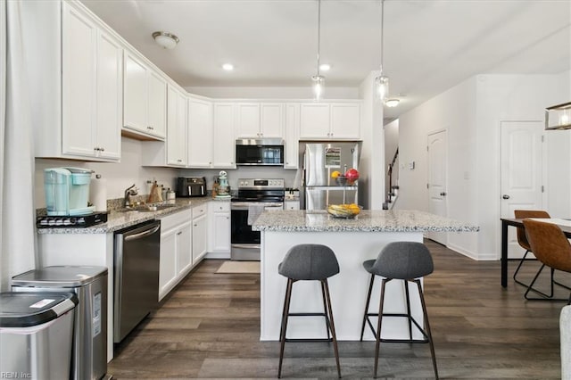 kitchen featuring stainless steel appliances, white cabinets, a kitchen island, pendant lighting, and dark wood-type flooring