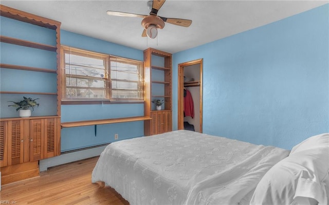 bedroom featuring a spacious closet, ceiling fan, light hardwood / wood-style floors, a closet, and baseboard heating