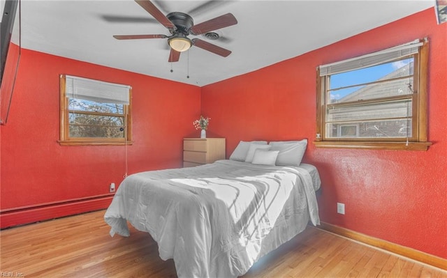 bedroom with a baseboard heating unit, ceiling fan, and wood-type flooring