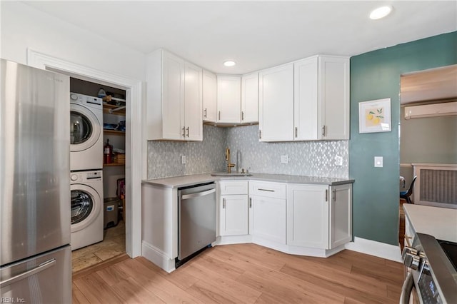 kitchen with appliances with stainless steel finishes, light hardwood / wood-style floors, stacked washer / drying machine, white cabinets, and sink