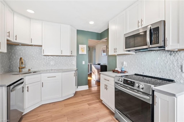 kitchen featuring sink, white cabinetry, light hardwood / wood-style flooring, decorative backsplash, and appliances with stainless steel finishes