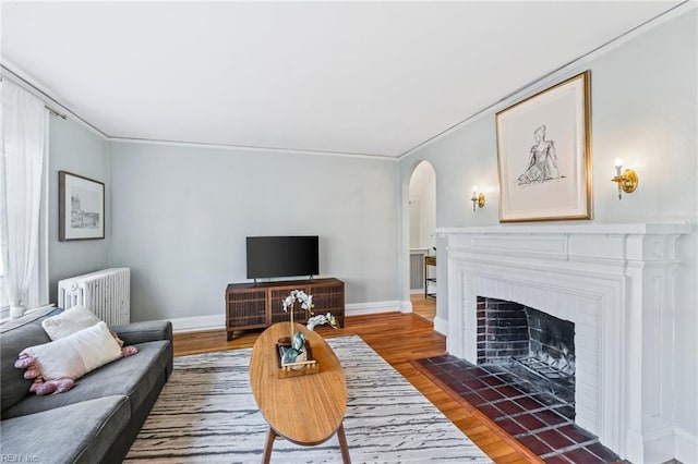 living room featuring radiator, a fireplace, crown molding, and dark hardwood / wood-style floors