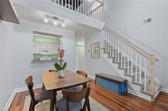 dining space with a towering ceiling, ornamental molding, and dark hardwood / wood-style flooring