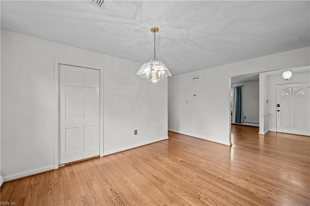 empty room with light wood-type flooring, a chandelier, and a baseboard heating unit