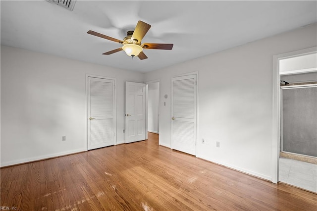 unfurnished bedroom featuring ceiling fan, light hardwood / wood-style floors, and two closets