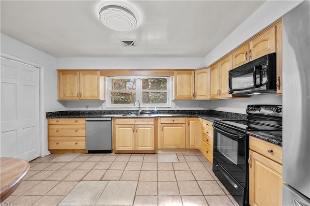 kitchen featuring dark stone countertops, black appliances, sink, light tile patterned flooring, and light brown cabinets