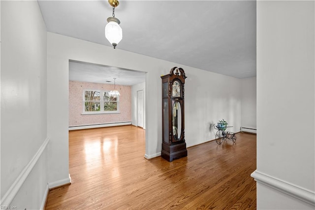 unfurnished living room featuring hardwood / wood-style flooring, a baseboard heating unit, and a chandelier