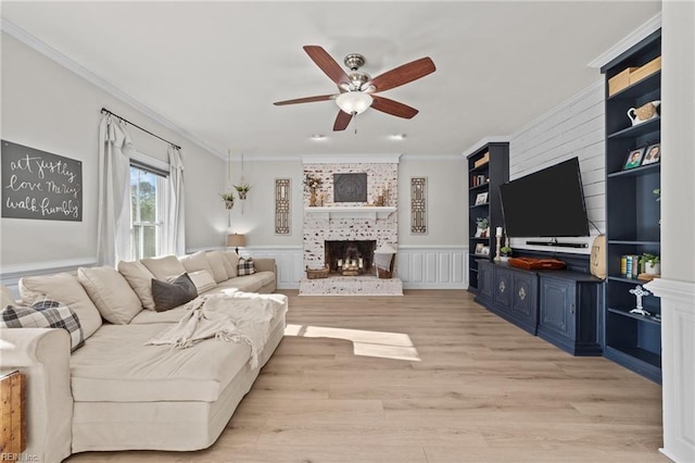 living room with ornamental molding, ceiling fan, light wood-type flooring, and a brick fireplace