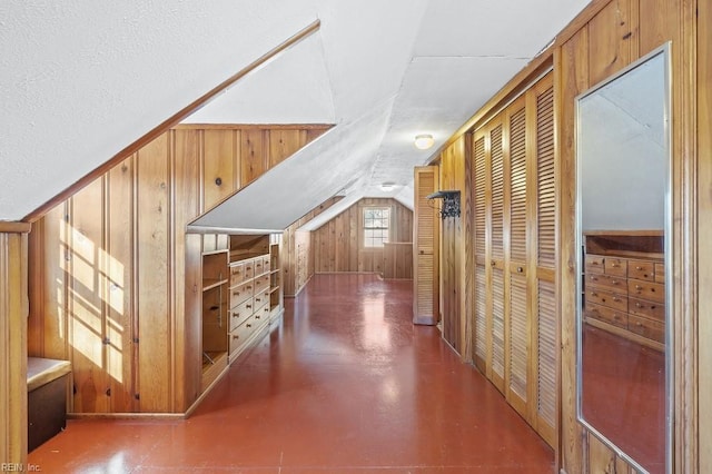 hallway with vaulted ceiling, a textured ceiling, and wooden walls