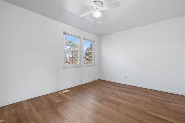 empty room with ceiling fan, visible vents, baseboards, and wood finished floors