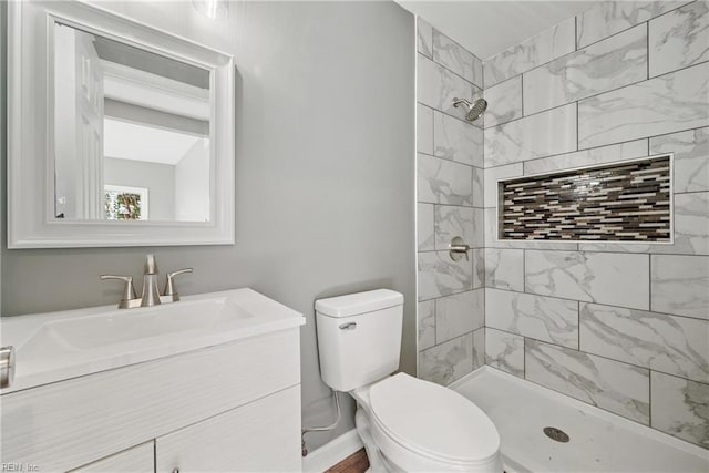 bathroom featuring toilet, tiled shower, and vanity