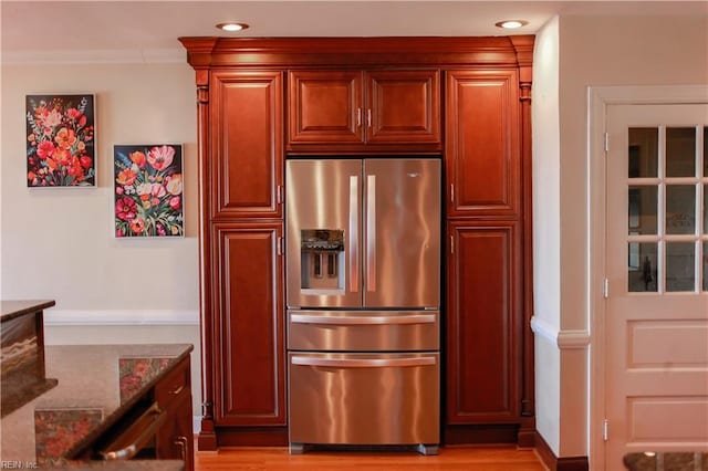 kitchen with ornamental molding, stainless steel fridge, light hardwood / wood-style floors, and dark stone countertops