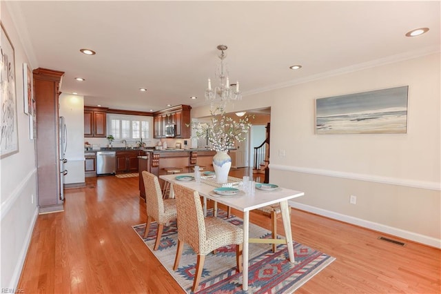 dining space with light hardwood / wood-style floors, a chandelier, crown molding, and sink