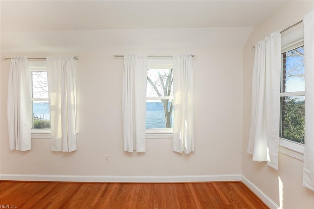 empty room with hardwood / wood-style flooring, vaulted ceiling, and plenty of natural light