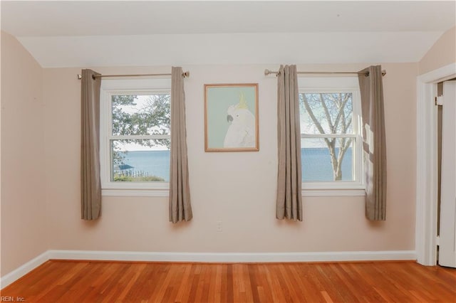 empty room featuring hardwood / wood-style floors, a water view, and lofted ceiling