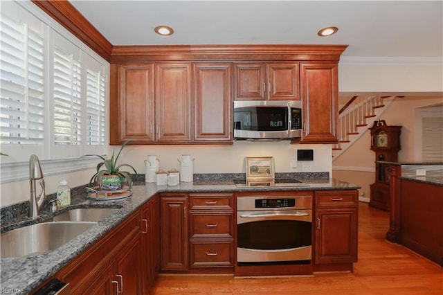 kitchen featuring stainless steel appliances, dark stone counters, light wood-type flooring, and sink