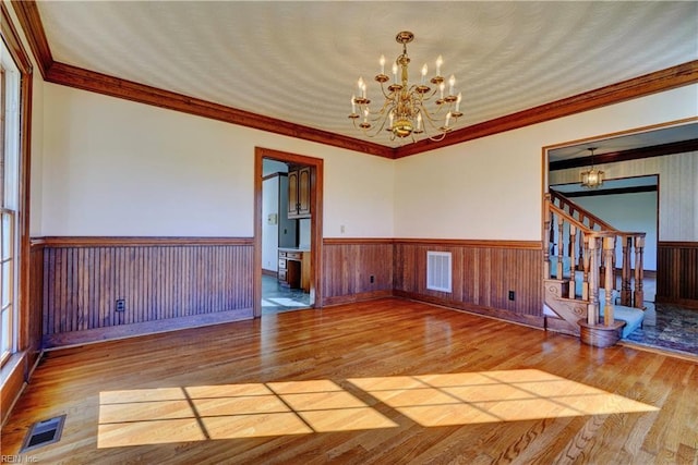 empty room with ornamental molding, a chandelier, and hardwood / wood-style flooring